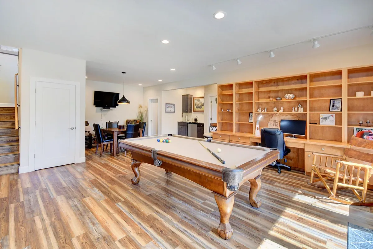 This image captures a vibrant lower-level space featuring a pool table as the focal point, a dining area nearby, built-in bookshelves, and an entertainment center. The setup showcases a multifunctional environment perfect for gaming, dining, working, and relaxing—all core themes of the section.