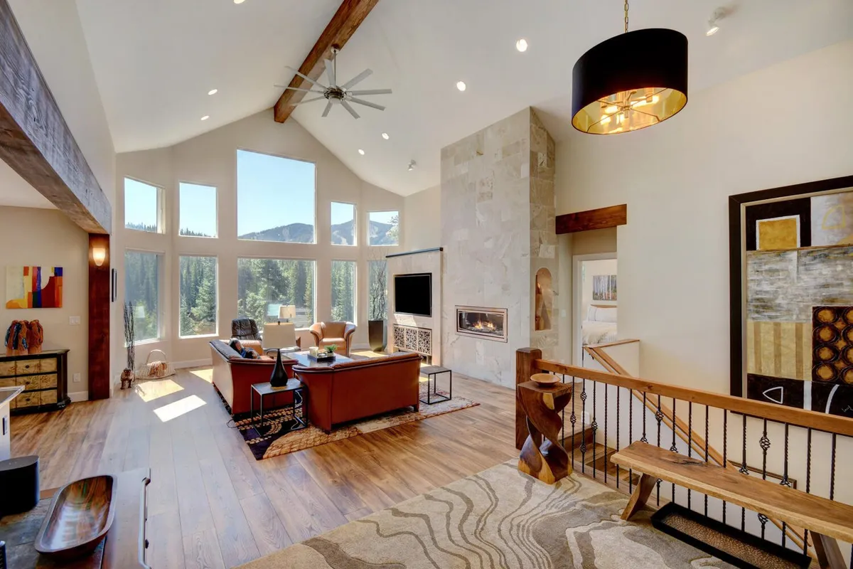 A stylish lounge area featuring a modern fireplace, large windows with spectacular mountain views, elegant furniture, and tasteful artwork on the walls. The scene evokes warmth and sophistication, perfect for unwinding after a day outdoors or gathering with friends beside the fire.
