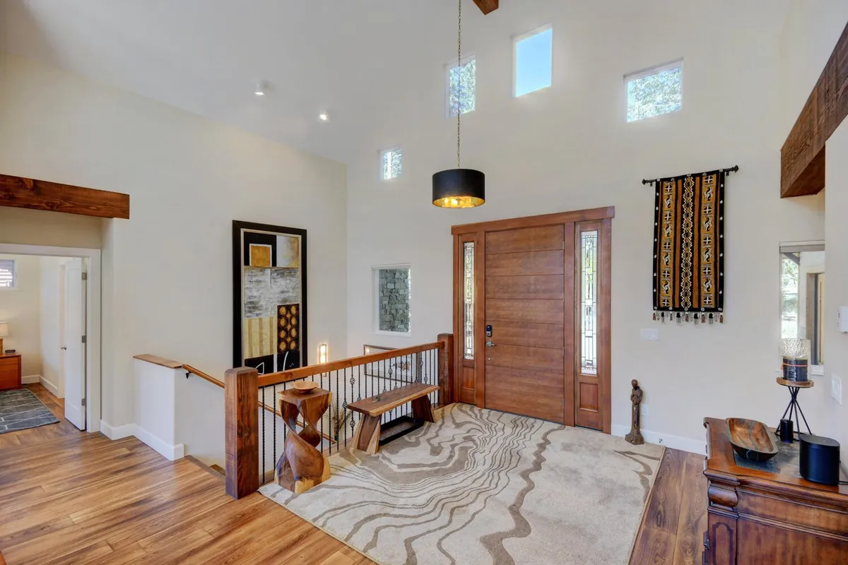 A grand foyer with a striking wooden front door, vibrant modern artwork on the wall, a textured area rug, and a contemporary hanging light fixture. The entryway radiates warmth and sets a stylish tone that welcomes guests into the heart of the home.