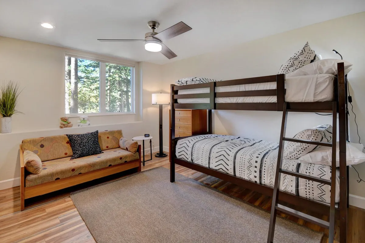 A playful and welcoming bunk room featuring a bunk bed, a cozy sofa, a large window letting in natural light, and a lamp. The space is designed for relaxation, reading, and shared fun among children or cousins.