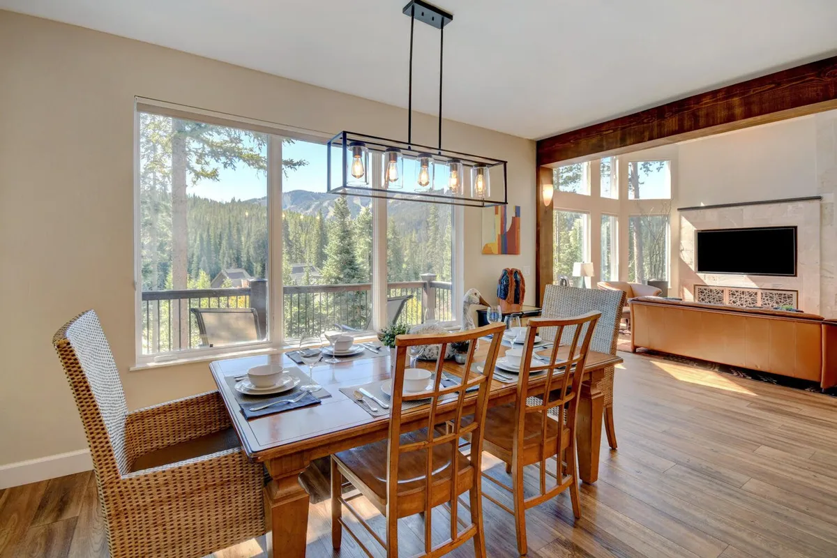 A dining area set for family meals and gatherings, with a large table placed in front of generous windows showcasing stunning mountain scenery. The modern light fixture and wooden cabinetry contribute to the space's welcoming and refined feel, ideal for gourmet meals and memorable celebrations.