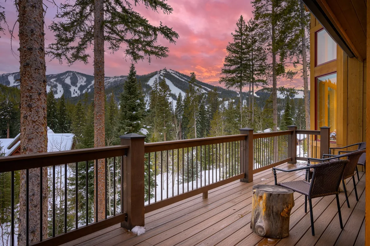 A serene exterior view from a deck overlooking majestic mountain vistas, with a sunset sky casting a golden glow. Comfortable deck furniture invites relaxation, suggesting the perfect spot for morning coffee, evening gatherings, or stargazing after a day of adventure.