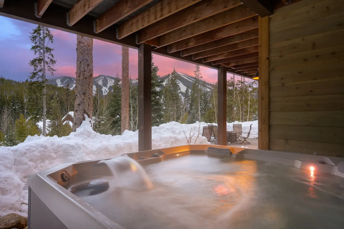 This exterior image showcases a bubbling hot tub set against a breathtaking snow-covered mountain landscape. Surrounding the hot tub is a cozy outdoor seating area, inviting guests to relax and socialize while gazing at the sunset or stargazing on clear evenings.